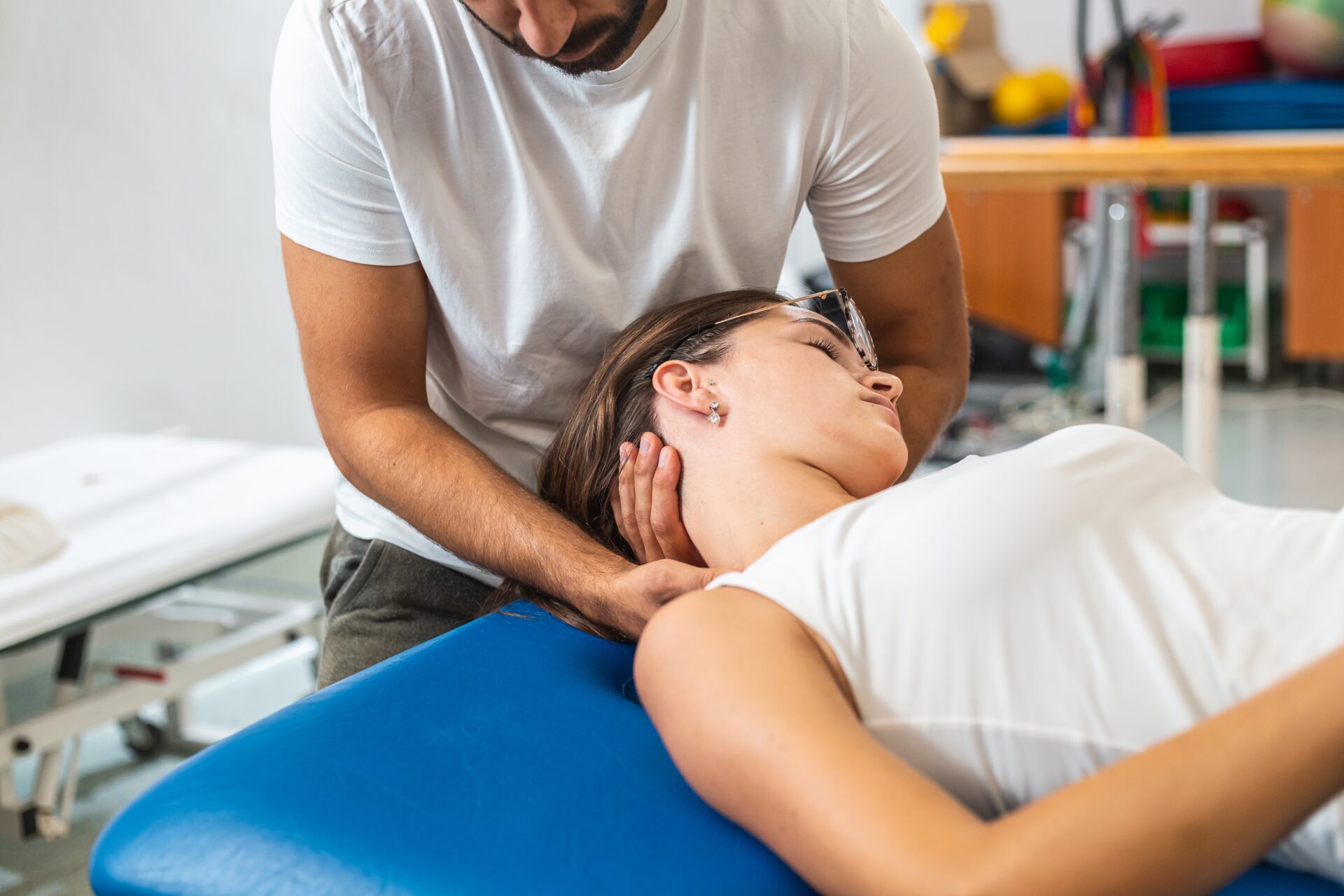 Close-up,Shot,Of,A,Male,Physiotherapist,Doing,Manual,Neck,Stretching A fitness instructor assists a woman practicing yoga in the Downward Dog pose, in a bright, spacious studio.